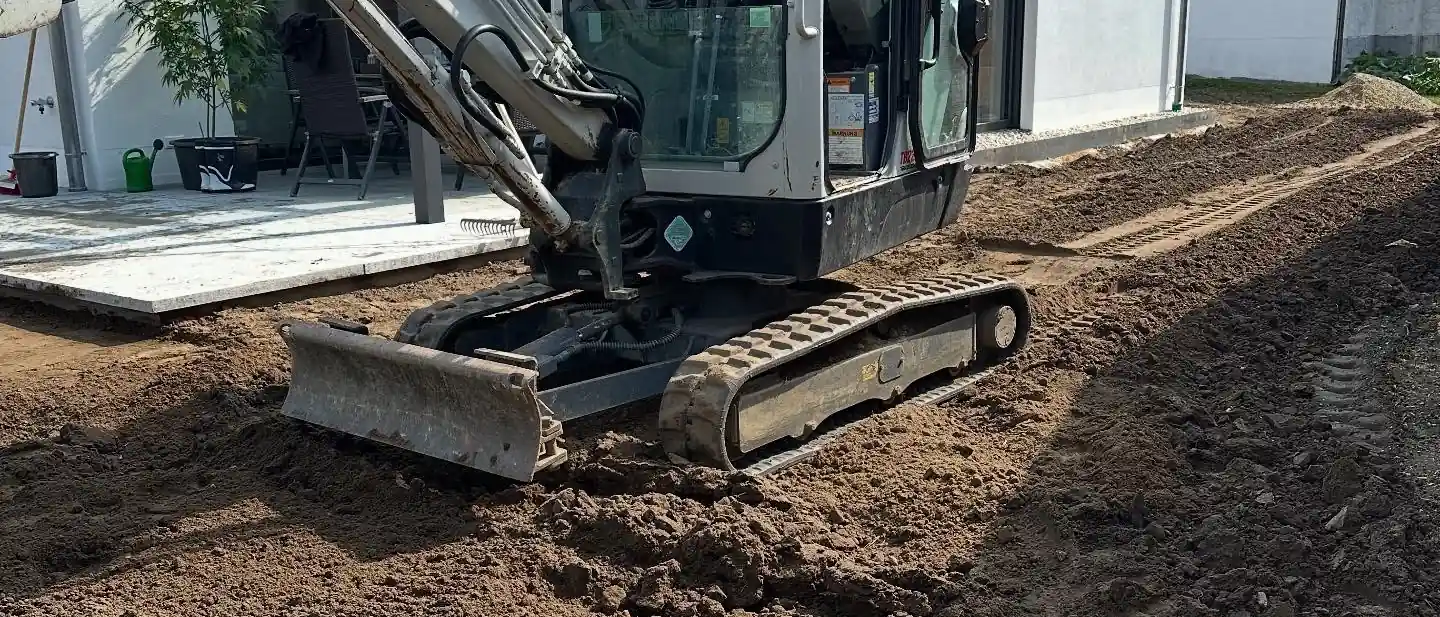 Minibagger beim Verteilen von Mutterboden auf einer Baustelle neben einem Wohnhaus