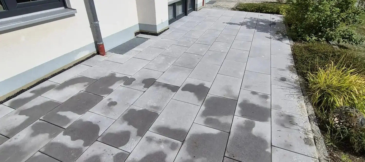 Terrasse aus großformatigen Betonplatten entlang der Hausfassade, rechts eine bepflanzte Beetfläche