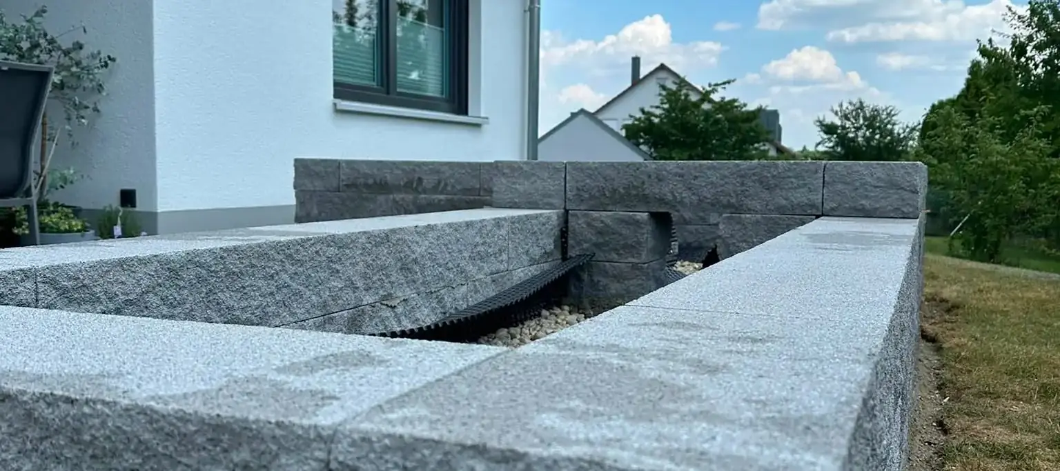 Hochbeet aus Granit-Blockstufen mit scharfer Kante und gleichmäßiger Fuge neben einem Wohnhaus