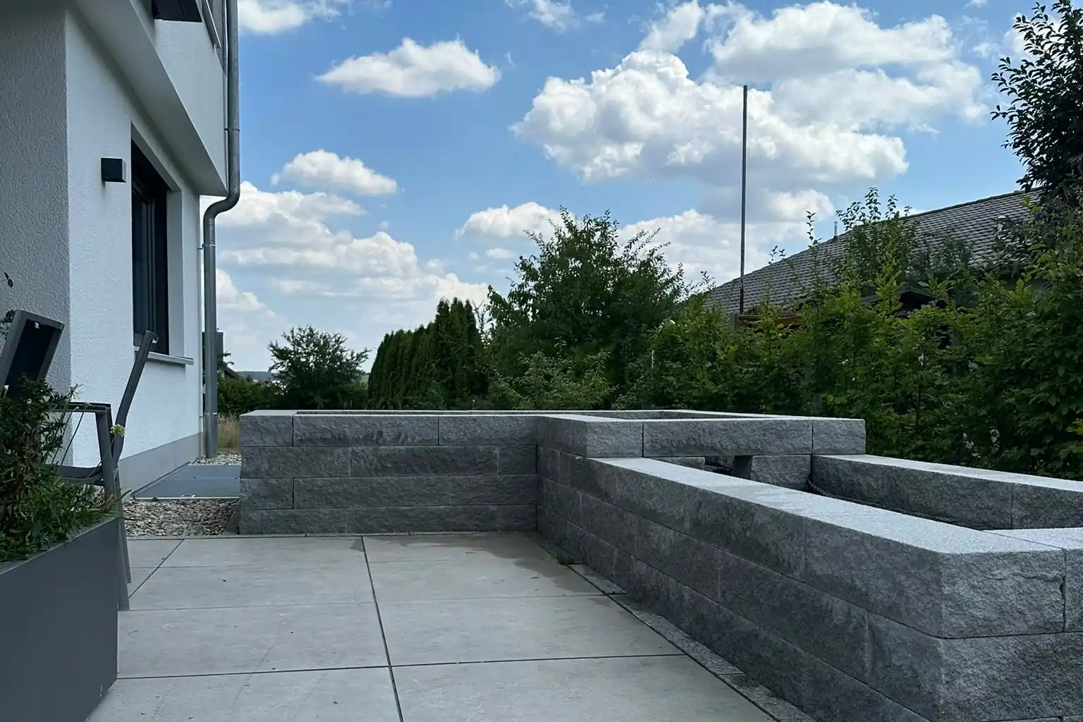 Zwei Hochbeete aus Granitsteinen an einer Terrasse aus großformatigen Betonplatten